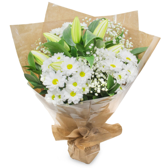 Presented upright against a crisp white backdrop, this hand-tied bouquet celebrates a restrained palette of white and verdant green with a feeling of quiet optimism. The composition centres on numerous white, daisy-like chrysanthemums whose concentric layers of slender petals open around subtle yellow centres, giving the arrangement a classic, friendly character. Alongside them rise slender lily stems with pale greenish-yellow buds: some remain tightly furled with gentle stripes on their outer petals, offering the viewer the promise of future blooms and movement in the days to come. Sprays of baby's breath (Gypsophila) are woven through the arrangement like soft exhalations, their tiny white florets lending an airy softness that contrasts with the fuller chrysanthemum heads. Lush dark foliage provides a grounding, evergreen frame and heightens the clarity of the whites beneath diffused studio light. The bouquet is finished in two layers of practical yet attractive wrapping: an inner sheet of crinkled brown kraft paper that brings a tactile, market-style warmth, and an outer clear cellophane that keeps the stems safe while letting the flowers' textures show through; the bottom is gathered and tied into a neat stand that speaks of careful hand-assembly. The scent is subtle and clean, a hint of fresh cut stems and petals. This arrangement reads as pure and consolatory - suitable for new beginnings, quiet celebrations, or expressions of sympathy - and would sit comfortably on a mantel in a cottage off Epping High Street or as a thoughtful delivery to neighbours near Connaught Waters.