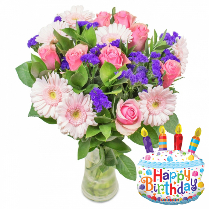 Set against a crisp white studio background, this festive floral ensemble pairs classic romantic blooms with a playful birthday balloon, arranged to read as both elegant and celebratory. A clear glass vase with a slightly widened base holds a generous gathering of stems so the water and verdant stalks are subtly visible, underlining the freshness. The bouquet's story is told in soft pinks: numerous pink roses - petals layered and velvety, ranging from gentle blush to a richer pink - form the arrangement's luxurious centre. Interlaced with the roses are pale pink Gerbera daisies, their broad rays framing honeyed, slightly darker centres that catch the eye. Sprays of vivid purple filler (statice/limonium) are woven through, their textured clusters adding depth and a slightly rustic crunch against the smooth rose petals. Lush, glossy greenery frames and supports the blooms, leaves of different shapes creating a natural silhouette. To the lower right a metallic cake-shaped Mylar balloon punctuates the scene: white frosted top with a blue piped border, multicoloured sprinkles, and four cheerful candles - purple, red, orange and blue - each with a flick of yellow flame. Happy Birthday arches across the front in bright, playful letters and the small 'KALEIDOSCOPE' brand name is visible at the base. The photograph carries a soft, early-morning glow that suggests this arrangement would be a fresh, thoughtful birthday delivery for someone in Epping - suitable for sending from the High Street to a home near the forest or as a centerpiece at a small family gathering.