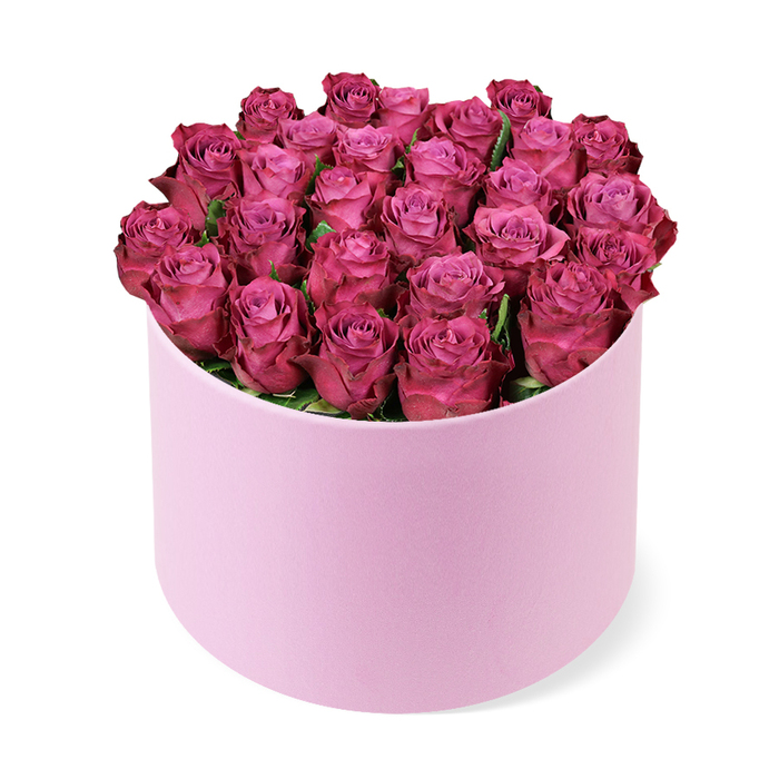 A sophisticated hat box floral design showcases a sweeping dome of deep fuchsia roses, captured against a clean, white studio background that draws all focus to the rich colours and gentle textures. Dozens of roses are packed so closely together that almost no gaps are visible, forming a perfectly rounded crown that spills just slightly over the edge of the container. The blooms are in early to mid-open stages, their petals unfurling in soft spirals that move from paler, rosy pink centres out to more saturated magenta and berry-toned edges, creating a natural gradient that adds depth and a sense of movement. Each petal appears velvety, with a delicate sheen that suggests freshness, as though the arrangement has been prepared this morning in a workshop just off Epping High Street. The cylindrical hat box is a light pastel pink with a smooth, matte surface that hints at a velour or satin-finished paper, offering a tactile contrast to the organic softness of the petals. A few small hints of deep green foliage peek between the rose heads, but they remain secondary to the sea of pinks and purples. Photographed from a slightly elevated angle, the composition reveals both the circular top of the arrangement and the upright form of the box, with a soft shadow underneath that anchors it in space. The overall impression is one of polished luxury and romantic warmth, reminiscent of a special gift delivered to a home near Epping Forest or a chic celebration in one of the local restaurants. This image suggests a grand, yet intimate floral gesture suited to anniversaries, Valentine's Day, milestone birthdays, or an elegant thank-you gift within the Epping area.