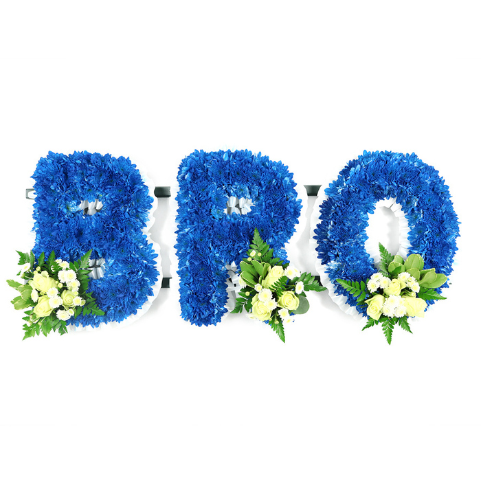 A solemn, meticulously made sympathy tribute photographed against a pure white studio backdrop: three large letters spelling out 'BRO', each letter built from thousands of tightly grouped royal blue chrysanthemum florets that create a smooth, sculpted form. The letters are constructed on a slim white support frame-likely floral foam-so the crisp white edge is visible around the negative spaces of the B and R and the inner circle of the O, signposting the arrangement's structural method and ensuring longevity during a service. Accenting each character are tasteful posies placed at strategic lower points: the B carries its cluster to the bottom-left, while the R and the O are graced with similar sprays to the bottom-right. These accents combine soft cream or pale yellow spray roses-some just unfurling, some in bud-together with small white filler blooms such as mini chrysanthemums or gypsophila, all set amid a mix of deep glossy leaves (salal or lemon leaf) and lighter, lacy fern fronds that add movement and depth. The saturated royal blue reads as both bold and peaceful; when paired with the gentle ivory tones the whole composition communicates respect, calm and an intimate memorial quality. Under diffused light the chrysanthemums show subtle petal shadows and a velveteen surface while the pale roses introduce a faint, comforting perfume. This piece is tailored for funerals and wakes common to Epping venues-suitable for chapel display near Epping Underground or for dedication by the edge of Epping Forest-and is intended as a dignified, personalised way to honour a brother's memory.