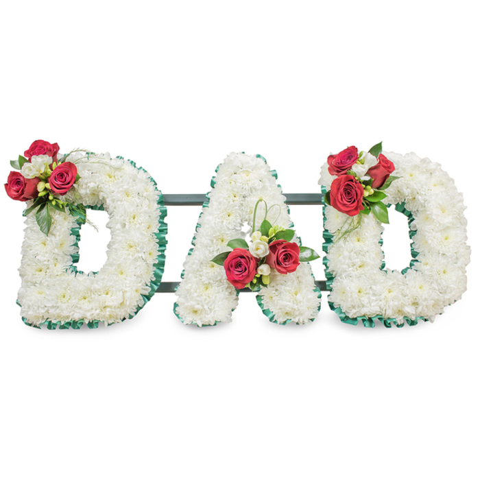 A carefully composed funeral tribute that spells out DAD in three large, sculptural letters, each face densely carpeted with hundreds of small white chrysanthemum blooms to produce a uniform, tenderly textured surface. The perimeter of every letter is edged with a deep emerald green pleated ribbon, its subtle sheen and crisp folds providing definition and an elegant contrast to the soft white flowers. On the upper left curve of the first 'D' a small, concentrated bouquet of fully opened deep red roses is artfully mixed with delicate white freesia and abundant dark green foliage, creating a focal point that draws the eye. The central 'A' carries a similar arrangement positioned near the base of its left diagonal, accompanied by a delicate loop of bright green foliage that rises gently to suggest movement and life. The final 'D' mirrors the first with a complementary spray of red roses, white freesia and verdant leaves on its upper right curve, giving the whole composition a pleasing symmetry. Slim dark green or black support bars are discreetly visible behind the letters, ensuring stability for display at a service or graveside. Photographed against a bright white background with soft, even lighting, the piece communicates purity, respect and heartfelt remembrance - white chrysanthemums for devoted love and red roses for deep affection. This is the sort of considered, personal tribute often requested for fathers' memorials in the Epping area, including services near the High Street or along the edges of Epping Forest.