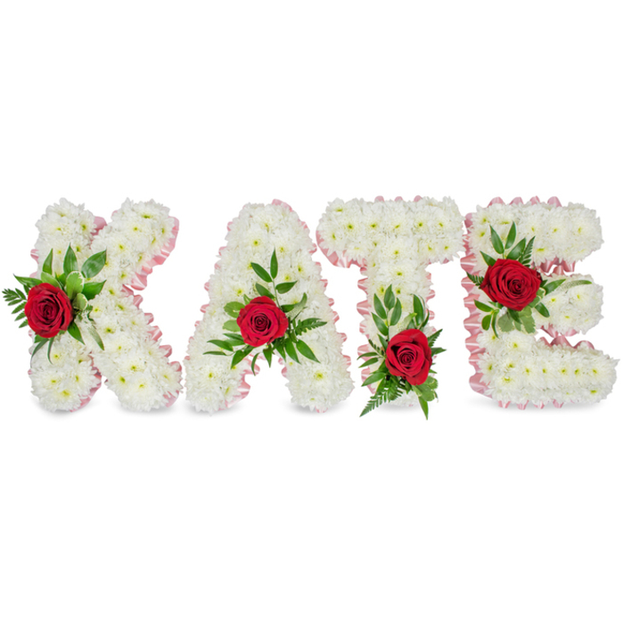 A dignified floral name tribute spells out KATE in tall, block letters fashioned entirely from compact clusters of pure white chrysanthemum heads, producing a soft, cloud-like surface that suggests purity and calm. Each letter is edged with a fine pale-pink satin ribbon that gently follows the outer contours, its subtle sheen catching the soft light and lending an elegant outline to the otherwise monochrome forms. A solitary deep-red rose is placed on the face of each character, its velvety petals standing out sharply against the snowy chrysanthemums; lush green foliage - broad leaves and delicate fern fronds - nestles the roses and adds natural movement and depth. The florist's placement is deliberate: the rose and greens rest on the lower left vertical of the 'K', the 'A' bears its rose at the apex of the triangle, the 'T' is highlighted at the base of the left side of its crossbar, and the 'E' is marked at its central horizontal arm, giving the whole name a balanced, readable rhythm.

Presented on a plain white background and touched by even, diffused lighting, the arrangement reads as both an artistic composition and an intimate memorial offering. The colour story-white chrysanthemums, pale-pink ribbon, deep-red roses and verdant greens-carries a traditional vocabulary of sympathy: innocence, gentle affection and enduring remembrance. As a floral design made for farewells and commemorations, it sits comfortably among other tributes yet retains a personalised presence, clear and respectful.

For local families in and around Epping, such a bespoke letter arrangement can be tailored to chapel dimensions or placed on the church steps, designed to communicate a name with clarity and tenderness at a funeral or celebration of life.