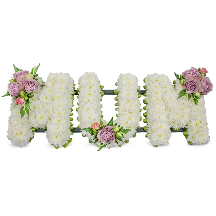 A lovingly made tribute spelling MUM in large, free-standing letters, entirely covered in thousands of small, fresh white chrysanthemums that create a soft, even surface reminiscent of a downy white blanket. The close-packed blooms reflect cool, steady light, producing a serene, almost luminous effect that feels respectful and calm. Three tasteful accent clusters of soft lavender roses and pale pink rosebuds have been artfully positioned to catch the eye: one graces the upper left arm of the first 'M', another nestles in the central curve of the 'U', and the last sits on the upper right arm of the finishing 'M'. The roses range from open blooms to tight buds, offering both the fullness of memory and the delicacy of a private sentiment; their gentle fragrance is suggested rather than overpowering. Fresh, vibrant greenery - slender fern fronds and lighter green leaves - weaves through the composition, adding contrast, movement, and natural depth against the white chrysanthemum field. A dark green structural element, possibly a ribbon-wrapped bar or mossed foam base, is visible at the letters' bases, providing discreet support and a clean line that unites the trio. Presented against a pristine white background, the arrangement conveys peace, reverence, and the quiet dignity of a mother's memorial. As an Epping florist familiar with local funerals near Epping Forest and the High Street chapels, Flowers Epping (flowersepping.info) would describe this piece as a tender, traditional choice - perfect for a funeral service, wake, or graveside dedication where the family wants a calm, loving statement of remembrance.