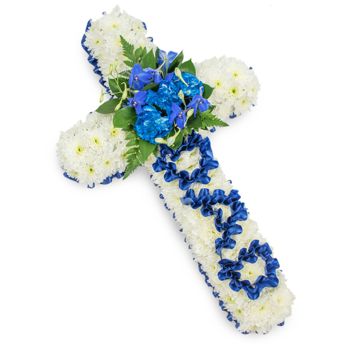 A visually striking funeral cross arrangement is presented on a bright white background, allowing its colours and craftsmanship to be clearly appreciated. The cross itself is fully padded with a dense blanket of pristine white spray chrysanthemums, each head carefully angled so the petals overlap, creating a seamless, cushion-like texture that looks soft to the touch. This snowy floral surface is framed all around by a deep royal blue satin ribbon, meticulously pleated and secured along the edges of every arm and the vertical stem. The ribbon's subtle sheen catches the light, giving the tribute a refined, ceremonial feel often chosen for services in and around Epping's churches and crematorium. At the central junction of the cross, a lush cluster of royal blue flowers forms a bold focal point. Full, ruffled blue carnations, possibly supported by slender spires of blue delphiniums or orchid-like blooms, rise gently from the white base, creating height and visual interest. Dark green fern fronds and selected foliage are woven through this spray, their feathery and glossy textures bringing natural depth and balance to the intense blues. Down the vertical arm of the cross, the word DAD is cleverly shaped from the same royal blue satin ribbon, with each letter looped and folded by hand so that it sits in low relief against the white chrysanthemum cushion, clearly legible yet still harmonious with the design. Soft, even lighting casts a delicate shadow around the outline, emphasizing the cross's three-dimensional form. This floral tribute, typical of what a skilled local florist in Epping might create, expresses profound love, remembrance, and respect for a father, making it a fitting choice for funeral processions, church services, and graveside tributes throughout the local area.