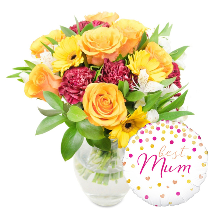 A rich and celebratory floral composition sits against a pristine white background, artfully staged to highlight texture, colour, and sentiment. Prominent peachy-orange and sunlit yellow roses anchor the arrangement, their rounded, velvety petals layered in classic spirals that catch light and suggest both elegance and comfort. Bright yellow gerbera daisies punctuate the scene with their broad, cheerful faces and deep-centre contrast, while ruffled burgundy carnations build volume and a sumptuous, tactile shadow-play among the blooms. White alstroemeria with slender petals and faint freckling weave delicately through the warmer tones, offering a refined, almost lyrical accent. A plentiful underlayer of glossy green foliage-smooth broad leaves and narrow sprigs-gives structure and a breath of freshness, and the clear glass vase reveals the crisscrossed stems and clean water inside, a quiet testament to careful conditioning and florist technique.
To the lower right, overlapping the base of the vase, a round white foil balloon adds a playful flourish. It is festooned with scattered gold and fuchsia dots and small heart motifs, and the centre reads best Mum in an elegant, flowing fuchsia script that feels personally written. The overall effect is warm and thoughtful, the sort of bouquet-and-balloon pairing one might send to a mother after a walk in Epping Forest or a relaxed morning coffee on Epping High Street-a present that says appreciation, celebration, and homegrown affection.