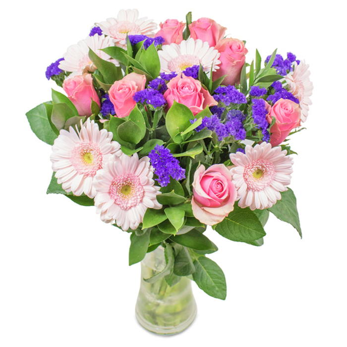 An exquisitely arranged bouquet sits in a clear glass vase, its features vivid against a clean white backdrop - a hallmark of refined Epping floral design. The focus rests on seven to nine pink roses in various stages of blossom, some petals still gracefully curled, others unfolding into classic spirals that catch the light. These regal roses are partnered by five to seven pale pink gerbera daisies, their generous, layered blooms and almost-white centres radiating a soft pastel glow reminiscent of the tranquil borders found in local Epping gardens. Sprinkled throughout, clusters of vibrant purple statice introduce playful depth and a lively pop of deeper tone, their petite blooms adding both texture and energy. The abundant base of dark green foliage enhances the natural freshness, suggesting a morning harvest from the nearby Epping countryside. Seen through the crystal-clear glass, stems and cool water promise lasting vitality-ready to be delivered as a thoughtful birthday present, a meaningful Mother's Day gift, or a joyous centrepiece for a home in Epping or the surrounding villages. This arrangement captures both celebration and affection, conveying a sense of welcome, beauty, and community spirit cherished throughout the area.