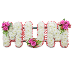 A deeply respectful funeral tribute spelling MUM in three connected capital letters, handcrafted from a blanket of pure white chrysanthemums that create a soft, uniform texture across each letter. The blooms are small and densely packed so the shapes read clearly even from a distance, while a delicate ruffled pale-pink ribbon hugs each outer edge and gives a whisper of warmth to the composition. You can see the dark green structural frame peeking between the letters - the discreet support that allows this standing tribute to be placed at a church entrance or beside a graveside. Three decorative clusters of accent flowers break the white with loving colour: fuchsia-pink roses in tight posies sit on the upper left of the first M, at the inner curve of the U, and on the upper right of the last M, each accompanied by glossy fern-like foliage and coral hypericum berries that catch the light. The contrast between the crisp mums and the velvety roses creates a tactile harmony, and there is a faint, comforting scent of fresh blooms when you are close. As a florist serving Epping and the surrounding villages, I imagine this piece displayed at a service near Epping High Street or in the peaceful chapel by the forest; Flowers Epping can prepare arrangements like this with careful attention to scale and finish for a memorial, wake, or graveside dedication, offering a quietly comforting tribute that honours a mother with dignity and tenderness.