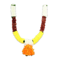 This U-shaped decorative mala is a small study in colour rhythm and cultural purpose, presented on a clean white background so every texture and hue is clear. At the narrow tops, compact clusters of off-white petals form a delicate crown - soft, cushiony blossoms like miniature chrysanthemums whose pale tones bring a quiet, ceremonial light. Immediately beneath, bands of warm reddish-brown provide weight and contrast; their flattened, layered texture resembles dried pod or leaf shapes, lending an autumnal depth that steadies the brighter tones below. The sweeping arms resolve into a broad expanse of vivid yellow, densely packed and fluffy, unmistakably recalling marigolds used across Hindu rituals for their auspicious cheer. Suspended at the centre is a large, voluminous orange tassel: ruffled, multi-layered petals gathered into a single, luminous pendant that anchors the garland and draws the eye. Tiny green touches at the joins act as subtle leaf-like separators, adding compositional clarity. The garland's artificial construction - fine fabric fibres and tight threading - promises durability, suitable for repeated use during Diwali, Pongal, Onam or wedding decorations, and for hanging over home altars in the Epping area. In my florist's view the piece balances solemnity with celebration: the creamy whites suggest reverence, the russet and yellow bring warmth, and the central orange offers joyful focus. I picture it brightening a doorway on Epping High Street during festival evenings or hanging in a family home near Epping Forest, where the colours will read both traditional and modern under soft indoor light.