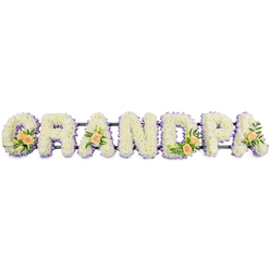 The floral tribute in this image presents the word "GRANDPA" as a long, horizontal line of sculpted letters, each one standing proud on a low, dark bar that disappears against the clean white background. Every capital is densely packed with fresh white spray chrysanthemums or similar small blooms, their overlapping petals creating a cushiony, almost velvety surface that looks soft to the touch. Around the perimeter of each letter runs a narrow band of pale lavender or lilac flowers, adding a gentle wash of colour and clearly defining the shapes so they are easy to read even from a distance. The cool whites and purples evoke peace and quiet reflection, making this a fitting piece for a funeral or memorial service. To break the expanse of white, the florist has woven in clusters of peach-toned roses and rich green foliage. A generous spray decorates the curve of the G, with several open roses, tight buds, and slender white lily buds rising delicately above the cushion of chrysanthemums. Smaller, coordinated clusters sit on the first A, the central D, and the final A, drawing attention to key points along the tribute and adding warmth and human tenderness to the serene design. This is the sort of personalised funeral arrangement a family in Epping might choose to have delivered to a church near the High Street or to a service on the edge of Epping Forest-a crafted, thoughtful way to say goodbye to a much-loved grandfather, combining traditional floristry skill with quiet emotional resonance.