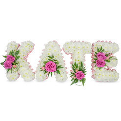 A sculpted, personalised floral display spells 'KATE' in substantial, three-dimensional block letters, each letter formed from hundreds of small, immaculate white chrysanthemums that create a seamless, cloud-like texture. A soft pale-pink satin ribbon neatly outlines the inner edges of every letter, giving definition and a whisper of blush against the white base. Bright hot-pink roses act as vivid focal points: a pair of opened pink roses on the K's left arm, a single prominent rose cradled low in the A, a lone vivid rose at the base of the T, and two roses accenting the right side of the E. Between these focal clusters sit delicate pink spray blooms, light alstroemeria highlights and varied greenery - ruscus, ferny fronds and variegated leaves - that lend contrast, depth and a natural garden freshness.

Presented freestanding on a pure white background with subtle shadows that emphasise its three-dimensional form, the tribute reads as both refined and heartfelt; the roses give a gentle, familiar scent while the chrysanthemums keep the overall tone calm and dignified. This elegant, personalised memorial piece is frequently chosen for funerals or celebrations of life in and around Epping, Station Road chapels and nearby Theydon Bois. Prepared with local care by Flowers Epping and available for delivery across Epping and surrounding villages via flowersepping.info, it offers a tender, bespoke way to honour a loved one.