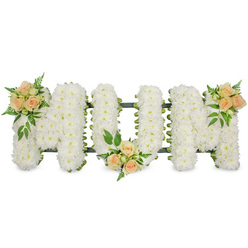 The image shows a refined funeral flower tribute that clearly spells out "MUM" in three bold, capital letters, all aligned in a straight line as if resting on a low stand. Each letter is densely packed with pristine white spray chrysanthemums, their small, rounded petals overlapping so closely that the surface looks like a soft, continuous cushion of bloom. Tiny shadows between the florets add subtle depth, while glimpses of dark green backing and ribbon edging trace the outlines, giving the letters structure and definition. To break the expanse of white and add a tender warmth, delicate accents of roses in soft peach and blush pink are arranged in three thoughtfully chosen places: at the top left of the first M, at the base of the U in the centre, and at the top right of the second M. These rose posies contain a mix of buds and half-open flowers, their spiral centres gently unfurling, surrounded by sprigs of rich green foliage and feathery ferns that curve naturally outwards. The whole composition is set against a clean, white background, which makes the colours and textures stand out without distraction. It feels like a tribute you might see at a quiet chapel in Epping, perhaps on the way to a service near the High Street or close to the edge of Epping Forest, where families gather to say goodbye. The design conveys calm, dignity, and gratitude for a mother's care, suggesting a message of peaceful rest and loving remembrance in every petal and leaf.
