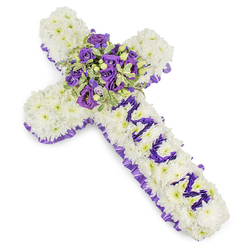 Presented on a stark white background to emphasise its precise craftsmanship, this cross-shaped sympathy tribute is built from countless white chrysanthemum blooms that create a seamless, cushion-like surface of purity and repose. The chrysanthemums are tightly placed so the cross reads as a unified whole rather than a collection of stems, giving the design solidity and a tactile softness that invites a gentle touch. Framing the piece, a ruffled purple satin ribbon traces the outer edge in a steady band of colour, the rich hue bringing an air of solemn elegance to the overall composition.

At the focal point, a compact but abundant central spray gathers deep violet and lavender roses with pale purple lisianthus, the roses' denser petals contrasting with the lisianthus' ruffled shapes to create depth and movement. Sprigs of variegated foliage-leaves with pale margins and darker centres-are woven through the cluster, adding light, structural highlights and a sense of fresh greenery; occasional small green berries introduce a subtle textural counterpoint. The vertical arm bears the word MUM spelled in smaller purple flower heads, the lettering deliberate and legible against the white field to make the sentiment unmistakable.

As a local florist familiar with Epping High Street and quieter corners near Epping Forest, I picture this design placed by a church door or on a graveside; it reads as a respectful, consoling piece. There is an understated fragrance and a calming palette that together offer solace while honouring a cherished life. Flowers Epping prepares such tributes for memorial services across Station Road and the surrounding community, always mindful of tenderness and detail.