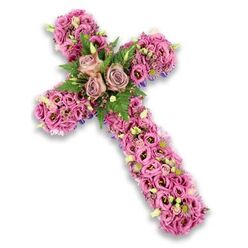 A graceful, three-dimensional floral cross is presented against a clean white background, its subtle shadow suggesting the piece might be resting on a chapel pedestal or easel in Epping. Every part of the cross is filled with flowers, from the tip of the top arm down to the base, creating a continuous surface of soft pinks, mauves, and light purples that feels almost like a quilt of petals. At the central meeting point of the arms, three large roses in a refined dusty rose shade form the emotional core of the design, their velvety petals layered in spirals that seem to open slowly and thoughtfully. Around these roses, feathery green ferns and smaller, darker leaves act like a natural halo, enriching the palette and giving the eye a place to rest. Flowing outward, the arms are densely set with lisianthus blossoms, each one trumpet-shaped and gently ruffled at the edges, shifting from light blush pink to more saturated berry tones with some blooms featuring darker, velvety centers that add depth. Between them, petite clusters of tiny pink and purple flowers, small white stars of blossom, and pale green buds flicker through the design like moments of shared memory. Along the edges, slim hints of deep purple ribbon or fabric framing peek through behind the flowers, lending structure and a touch of formality. The overall impression is serene and heartfelt, perfectly suited as a funeral cross or memorial tribute for services held around Epping, from quiet gatherings near the High Street to more traditional ceremonies in nearby parish churches, offering gentle comfort and a visible symbol of faith and remembrance.