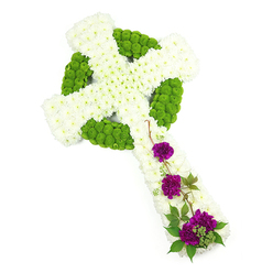 In this image, a carefully arranged Celtic cross floral tribute rests against a pure white background, its form crisp and unmistakable. The main shape of the cross is created from countless small white chrysanthemum blooms, wired and set so close together that they form a smooth, padded surface with a subtle curve along the arms and stem. These white petals, soft and slightly feathery, give the impression of purity and peace, like quiet snowfall over the streets leading from Epping High Road. Woven into the centre and circling the intersection of the arms is a bold pattern of lime-green button chrysanthemums. These compact, globe-shaped flowers are used with precision to draw out the circular halo and knot-like motifs distinctive to a Celtic cross, their spring-green tone bringing a sense of life, renewal, and gentle hope. At the lower section of the cross, three groupings of rich purple carnations sit in a graceful diagonal, each head full, ruffled, and almost velvety to the touch. They provide a heartfelt pop of colour, symbolising love and remembrance. Fine stems of deep green foliage and slender, twisting vines thread through and around these carnations, softening the outline and echoing the natural growth you might see along paths towards Epping Forest. The overall composition is dignified and serene, a handcrafted funeral tribute suited to honouring Irish or Scottish heritage or Christian faith. It would sit beautifully in a memorial service at a local Epping church or crematorium, or be delivered with sympathy to a grieving family as a visible expression of respect and enduring memory.