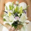 This enchanting bridal bouquet, designed in Epping and held by a bride bathed in gentle morning light, weaves a poetic tapestry of white and purple blooms. The pure, star-like Oriental lilies stand resplendent, petals silk-smooth and lightly freckled, exuding an air of purity and devotion that perfectly complements a ceremony at All Saints' Church. Clustered alongside, lisianthus blossoms edged in soft lavender evoke a sense of playful elegance, their subtle ruffles mirroring the delicate mist often seen hovering over Epping Green. Royal purple Veronica adds dramatic flair and textural intrigue, spiraling between airy baby's breath that gives the bouquet a dreamy, cloud-like softness. Embracing the flowers are spirited green accents-from broad leaves to feathery asparagus-that punctuate the arrangement with freshness. The bride's gently curved hands, manicured with a soft sheen, hold the stems with anticipation, and her white strapless dress melts into the background, leaving the bouquet shimmering at centre stage. The artistry and harmony of this bouquet tell a story of new beginnings and heartfelt vows, echoing the hopes of couples who wish to celebrate their love in the scenic serenity of greater Epping. This is more than just a collection of blooms; it is a tribute to both craftsmanship and the enduring beauty that local florists bring to wedding days throughout Essex.