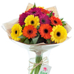 A joyful burst of colour lights up this Gerbera daisy bouquet, thoughtfully arranged by a local Epping florist and presented against a clean, luminous backdrop. Housed in a sleek, clear glass vase, the ensemble features a lively mosaic of blooms: radiant yellow, fiery orange, and compelling magenta petals, each surrounding a bold, dark centre that provides crisp contrast. Lush green leaves are interspersed among the flowers, offering a fresh, natural texture reminiscent of the trails around Epping Forest and the vibrant greenery seen near Lindsey Street. The arrangement is expertly bundled in rustic kraft paper and encased within a protective layer of transparent cellophane, its sheen reflecting soft daylight streaming in from a local shop window. The visible stems rest in sparkling water, bound together by a wrap of textured twine, from which a petite gift tag dangles-perhaps awaiting a special message or occasion. Every detail, from the carefully selected blooms to the artisanal touches, hints at thoughtful preparation and the pride of a local business. Ideal for infusing joy into celebrations, brightening a loved one's day, or as a cheerful centrepiece for gatherings in homes across Epping, this bouquet stands as a graceful expression of connection and craft. The vibrant harmony of colour, crisp presentation, and gently rustic accents embody the unique spirit and welcoming beauty found within the Epping community.