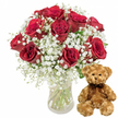 This clean, white-background image showcases a classic pairing often chosen by romantic customers in Epping: luxurious red roses and a cuddly teddy bear, presented together as a single, heartfelt gesture. On the left, a clear glass vase holds an abundant bouquet of about twelve deep red roses, each bloom rich with layered, velvety petals. Some roses are fully open, revealing their intricate spirals, while others are still gently cupped, suggesting freshness and the promise of continued blooming over the next few days. Nestled between the roses, airy white baby's breath forms a soft, cloudlike frame, its tiny blossoms creating a delicate, almost shimmering texture that lightens the composition and draws attention to the bold crimson tones. The vase itself is simple and elegant, allowing the eye to follow the straight green stems down into the clean water, giving the arrangement a sense of just-cut vitality, as though prepared in a local florist's studio close to Epping Station. To the right of the vase sits a medium-sized teddy bear made of light brown plush, positioned upright with its paws resting gently in front. Its fur appears fluffy and well-loved, with small black button eyes, a neatly stitched nose, and a subtle, friendly smile that suggests comfort and reassurance. Around its neck, a dark brown satin ribbon is tied neatly into a small bow, adding a touch of formality. The overall effect of the image is one of intimate celebration and tenderness, perfectly suited to anniversary surprises, Valentine's deliveries around Bell Common, birthday gifts, or spontaneous gestures of appreciation and love.