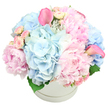 An abundant pastel floral arrangement rises from a round white hat box, photographed against a smooth, bright white background that emphasises its gentle colours. At first glance, the bouquet resembles a soft, blooming cloud, built from generous heads of light blue hydrangea and layers of pink peonies. The hydrangeas form cool, rounded clusters at the base and through the middle, their tightly packed tiny petals creating a plush, textured surface. Interspersed among them, the peonies display shades from baby pink to slightly deeper blush, some open and ruffled, others still in plump, promising buds. Light pink spray roses are tucked neatly between the larger blooms, their smaller buds and short stems filling gaps and adding a touch of intricate detail. Standing out with modern poise, two slender calla lilies in a stronger, almost fuchsia pink rise gracefully from the arrangement-one leaning towards the upper left corner of the composition and the other curving from the right-offering a subtle sense of movement and height. The flowers are packed closely, doming above the rim so that the bouquet looks both contained and luxuriously full. The pure white hat box has a minimal, slightly raised band around the top, with just the faintest glimpse of dark green foliage at the base of the flowers. Everything feels fresh, cool, and serene, like an early spring morning walk through Epping Forest when the air is still and hopeful. This arrangement suits a newborn celebration, a gender-neutral baby gift, a gentle condolence gesture, or a centrepiece for a pastel-themed party in an Epping home, reflecting quiet joy and thoughtful care.