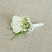 A single white orchid boutonniere rests on a softly textured, light beige fabric, its woven surface reminiscent of natural linen you might find in a cosy Epping High Street boutique. At the heart of the design sits a pristine Phalaenopsis orchid bloom, its broad, velvety petals a pure, luminous white that gently curves outwards. In the centre of the flower, the throat glows with the faintest touch of pale yellow and cream, adding warmth and depth, like early morning light over Epping Forest. Surrounding this central bloom is a delicate halo of baby's breath, each tiny Gypsophila flower forming a cloud-like ring of snowy white, giving the boutonniere a soft, airy feel. Threaded through and beneath these dainty blossoms, fine sprigs of feathery green foliage, likely asparagus fern or a similar light greenery, introduce fresh, vibrant tones and a whisper of woodland texture. The stems are expertly gathered into a slim, compact bundle and wrapped tightly in a smooth white satin ribbon, finished with a neat, understated bow that sits just below the orchid, ready to be pinned to a lapel. The overall composition feels calm, elegant, and timeless, perfect for a groom or groomsman at a classic Epping wedding, whether in a local church near Theydon Bois or a rustic venue on the edge of the countryside. The soft, even lighting and neutral background ensure every detail of the flower, foliage, and ribbon is clearly defined, highlighting the craftsmanship and quiet sophistication of this wedding boutonniere, ideal for formal occasions that call for subtle luxury and refined style.