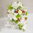 Set on a pristine white table beneath a soft, neutral beige backdrop, this luxurious table arrangement exudes the gentle opulence of a wedding morning in Epping. The flowers spill from a round white woven basket, its wicker texture tying the design to nature and hand-crafted care. At the core, several grand white lilies open in full trumpet form, their petals slightly curved back to reveal speckled throats and prominent stamens, suggesting a rich perfume. Close to the top centre sits a single pale cream-to-yellow rose, its layered petals forming a perfect rosette that glows warmly among the cool whites. From the right-hand edge of the basket, a sweeping cascade of white phalaenopsis orchids tumbles downward, each bloom with smooth, rounded petals and a gentle sheen, evoking the flowing line of a bridal cascade bouquet displayed on a top table at an Epping wedding venue. Around these main flowers, a lush halo of greenery and texture unfolds: fine grasses and ferns, more structured leaves, and bright green pom-pom chrysanthemums that add lively colour and touchable softness, reminiscent of mossy patches on a path through Epping Forest. Delicate sprays of white baby's breath soften the spaces between stems, while bright ruby-red berries gleam like small jewels, adding festive accents without disturbing the arrangement's serene mood. To the left of the basket, two decorative white woven orbs-a larger and a smaller-rest on the table, echoing the basket's pattern and giving the scene a modern, sculptural twist. The entire composition feels refined, fresh, and celebratory, ideal as a wedding table centrepiece or elegant feature for special occasions across Epping.