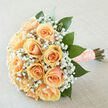 This bouquet presents a portrait of timeless tenderness: soft peach roses gathered in a rounded cluster, their creamy petals layered like silk and illuminated by soft, even daylight. Little clusters of white gypsophila float between the roses, creating a halo of delicate texture that makes each rose appear even more full and inviting. Rich, deep-green leaves provide an organic frame, their glossy surfaces and structural placement lending weight and elegant contrast to the pastel blooms. The stems are tightly wrapped in a textured blush ribbon, finished with pearl pins that add a quiet note of vintage glamour and invite the fingertips to linger. The photograph favours gentle, diffuse illumination so the bouquet's colour story - apricot, cream, and emerald - feels warm and natural rather than staged. Close your eyes and you can sense the fresh, green aroma of recently cut foliage mingling with the soft sweetness of roses and the barely-there powderiness of baby's breath, a scent profile suited to vows, renewals, or a refined wedding carried down the aisle from Epping High Street or after a ceremony at the parish. As a working shop that arranges locally, Flowers Epping composes pieces like this with both technical care and an eye for emotional resonance: a floristry keepsake that photographs beautifully and carries well through a day of celebration. The overall impression is one of calm joy and thoughtful craftsmanship, an arrangement meant to be both seen and remembered.