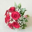 A lush, evocative bouquet rests serenely upon an off-white, lightly textured cloth, capturing the poetic romance of Epping's tranquil mornings. Its composition features approximately five or six plush, fully opened red roses, their deep crimson petals arranged in intricate spirals that draw the eye to each flower's tender heart. Mists of delicate, snow-white baby's breath weave between the roses, imparting a soft, weightless contrast that breathes life and lightness into the display. Wisps of dark green foliage, possibly broad-leafed ruscus or fresh eucalyptus, extend gracefully from the background, providing vibrant depth and a sense of flourishing abundance. The stems are expertly gathered and fastened at the base with an elegant combination of red and white striped ribbon and a fine strand of luminous pearls, a decorative flourish reflecting genuine care and artistry. The bouquet is bathed in gentle daylight, which enhances the rich reds, the pristine whites, and the nuanced greens, making every detail stand out in luminous clarity. Its classic, romantic style suits special occasions in Epping-weddings, anniversaries, and heartfelt celebrations-infusing each moment with the natural charm and local character that blooms throughout this vibrant Essex town. This arrangement, available for delivery from Flowers Epping, forms a perfect gesture of love and elegance for historic market days or intimate gatherings near Stonards Hill or Coopersale.