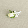 An elegant wedding boutonnière lies on a pale, woven fabric, its simplicity revealing layers of careful detail that a local Epping florist might fuss over before a ceremony. At the centre is a flawless ivory rose, its petals softly cupped, forming a gentle spiral of cream that suggests tenderness and calm. Surrounding the rose is a cloud of white baby's breath, each tiny flower like a star, giving the design a lace-like softness that contrasts beautifully with the rose's smooth, velvety texture. Slim blades of ornamental grass curve around the blooms, their deep green tones and gentle arcs lending a natural, slightly untamed feel, as if the flowers had been gathered from the edges of Epping Forest and then refined by skilled hands. The stems are neatly wrapped in smooth white satin ribbon, its surface satiny and taut, forming a slender, gleaming handle that would sit comfortably against a suit lapel. The little bow at the base is tidy and intentional, a final touch that reflects real care and precision. The neutral, linen-like background quietly frames the arrangement, allowing every curve and shade of ivory, white, and green to stand out without distraction. There is a sense of cool freshness and faint floral fragrance, like stepping out onto Epping High Street early on a wedding morning. Ideal for a groom, usher, or proud father of the bride, this boutonnière feels timeless and heartfelt, a miniature piece of wearable art that marks the importance of the day without ever shouting for attention.
