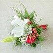 Beautifully arranged on a light beige, pebble-textured linen-like those found in sunlit Epping homes-this exquisite bridesmaid bouquet radiates elegance and joy. The star, a dazzling white lily, opens fully to reveal intricate reddish-brown speckles and golden anthers basking in gentle light. Embracing the lily's purity, a lush, crimson red rose unfurls its velvety petals, embodying tender romance seen at weddings across Epping. Delicate sprigs of white gypsophila create a gossamer softness, while bright red hypericum berries glisten amidst the arrangement, adding a vibrant festive contrast reminiscent of local festive markets. A slender pale green lily bud extends gracefully, a subtle promise of new stories to bloom. Enveloping it all, a textured palette of fine fern fronds and broader, lustrous green leaves enhances the bouquet's depth and organic charm. The neatly clustered stems are bound with a shiny red satin ribbon, uniting the hues in perfect harmony. Masterfully created for celebrations across the area-be it at St. John's or a gathering on Epping's High Road-this bouquet evokes warmth, love, and the timeless spirit of local floral artistry, making every moment it graces truly special.