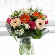 Brimming with the lively spirit of Epping, this bouquet is a symphony of rich hues and luxurious textures, artfully gathered to enchant the senses. At its heart, softly ruffled peach gerberas radiate warmth and comfort, their petals reminiscent of sunrise light over Market Place, while bold orange gerberas punctuate the design with bursts of joyful energy. Resting alongside, velvety magenta roses spiral inward with romantic intensity, their deep tones balanced by clusters of pristine white alstroemeria, which add delicate brightness throughout. Subtle pinks and sprigs of tiny white flowers interlace the larger blooms, creating nuanced layers and a feeling of generosity. Cradling the bouquet, broad aspidistra leaves are expertly folded, forming a polished border that sets off the saturated colours and ties the whole arrangement together. Around the flowers, pointed leaves and fine greenery contribute contrast and fullness. All converge in a tall, clear glass vase, showing off fresh green stems and lending the bouquet a sense of organic vitality. Bathed in gentle, diffuse daylight, every flower is lit to reveal its true vibrancy. Ideal for birthdays, thank-you gestures, or uplifting someone's day within the Epping community, this design sings with expert craftsmanship, seasonal beauty, and the heartfelt connection of local floristry.