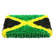 The photograph shows a bold rectangular floral tribute that reimagines the Jamaican flag as a deeply textured panel of fresh blooms. At first glance, the design reads like a piece of tactile artwork, with every inch covered in closely packed petals. A brilliant yellow saltire runs across the arrangement, sweeping diagonally from corner to corner. This X-shape is made from countless small flowers, their edges slightly curled to create a lively, sunlit effect, almost like a bright beam cutting through the composition. Between the golden arms of the cross, four neat triangles are formed. The upper and lower triangles are densely filled with verdant green flowers, recalling the lush greens seen around Epping's open spaces and forest walks after a shower. The side triangles are constructed from deep black blossoms, their velvety appearance lending an air of gravitas and quiet respect, essential to a piece intended for a funeral or memorial. The tribute has noticeable thickness, rising from its concealed base so that the flowers form a three-dimensional, cushion-like surface. Soft, even lighting reveals the minute ridges, folds, and shadows among the petals without washing out the rich colours. There are no ribbons or additional decorations; the focus remains solely on the strong geometry and cultural symbolism of the flag. This floral arrangement feels especially suited to honouring a loved one with Jamaican roots in Epping, whether delivered to a local funeral home or placed at a graveside ceremony, offering a moving blend of national pride, personal memory, and artisan floristry.
