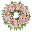 This image shows a lush, circular funeral wreath arranged flat on a clear white surface, photographed from directly overhead so the entire design appears as a complete, graceful ring. The wreath is densely filled with large, fully opened roses in elegant tones of dusty lavender, antique mauve, and soft, smoky purple, their many layered petals creating velvety spirals that lend a sense of depth and quiet luxury. Threaded between these statement blooms are clusters of smaller pastel pink spray roses, many at different stages of flowering, from tightly furled buds to softly opening blossoms. These petite roses bring a gentle warmth and tender detail, as if marking small, cherished moments within the larger circle of remembrance. All the flowers rest upon a substantial bed of rich, dark green ferns and structured foliage, the delicate, serrated leaves stretching outward to form a verdant halo that sharply contrasts with the soft floral tones. Subtle flecks of deeper greenery and tiny buds are tucked among the petals, providing dimension and the natural irregularities of a thoughtfully crafted piece. The even lighting highlights every texture, from the velvet of the petals to the crisp veins of the foliage, without casting harsh shadows, giving the wreath a calm, timeless presence. This kind of arrangement would be chosen as a loving tribute for a funeral or memorial in Epping, perhaps delivered to a service near the High Street or to a family home in a quiet cul-de-sac, where its gentle colours and circular form can symbolise unending love, remembrance, and peace.