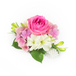 Set against a crisp white backdrop and bathed in soft, natural light, this compact corsage reads like a whispered promise of spring. At its center sits a lush, bubblegum-fuchsia rose, young and plush with tightly spiralled inner petals unfurling toward a fuller bloom; its velvety texture and saturated pink tone draw the eye and suggest warmth. Encircling the rose, clusters of pale pink and lavender hydrangea florets fold gently into one another, their papery layers adding airy volume and a romantic, garden-fresh softness. Nestled among these is a trio of creamy white, trumpet-shaped blooms-alstroemeria with delicate ruffled edges and subtle green throats-whose clean faces lift the palette and introduce a quiet, lily-like brightness. Glossy, broad evergreen leaves form a verdant cradle beneath the flowers, their cool sheen grounding the composition, while slim, upward-sweeping green buds flecked with pale yellow promise future opening and movement. At the lower right, a small cluster of luminous white pearls, varying slightly in size, cascades like a miniature heirloom, lending a satin gleam and an elegant punctuation to the arrangement. The overall effect is tactile and fragrant: cool petal surfaces, a faint sweet scent of rose and fresh-cut hydrangea, and the soft contrast of satin pearls against velvet bloom. Ideal as a bridal corsage, bridesmaid posy, or a refined boutonnière for prom or an anniversary, this piece evokes the gentle formality of Epping's springtime gatherings near Epping High Street and the hush of walks through Epping Forest, where delicate beauty feels both intimate and enduring.