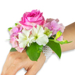 A delicate wearable bouquet captured against a clean white studio backdrop: a wrist corsage that reads like a quiet love letter to spring. At its centre sits a large, fully opened deep fuchsia-pink rose, its velvety petals layered into a tight, elegant spiral that catches the soft directional light and suggests a faint, warm fragrance. Around the rose, clusters of blush-pink hydrangea florets add a soft, cloud-like texture, their tiny petals overlapping to create gentle volume and a subtle watercolor effect. Scattered among those are pristine white alstroemeria (Peruvian lilies), each blossom revealing four to six smooth petals with pale green streaks at their throats, lending a fresh, crisp contrast to the deeper rose tone. A small cluster of pale green alstroemeria buds and a few nearly closed pink buds on the right promise future blooms and lend a sense of movement and expectancy.
Rich emerald green leaves cradle the arrangement, their broad glossy surfaces providing depth and a cool foil to the warm florals. The corsage is secured with a refined multi-strand bracelet of tiny lustrous white pearls that wraps around the wrist and extends partially across the back of the hand, the pearls catching the light with a soft sheen. The wearer's left hand and forearm, shown in a light-to-medium skin tone, anchor the piece and demonstrate scale and elegance. Ideal for prom, a first dance, or bridal parties, this design conveys careful florist craftsmanship and wearable beauty-a small, scented heirloom that would feel at home walking under the canopy of Epping Forest or arriving quietly for a family celebration on Epping High Street.